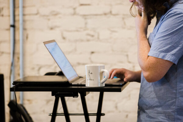 Man in blue shirt with coffee cup works on his computer