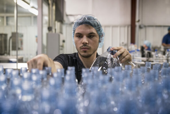 Man with hairnet sorts plastic bottles in manufacturing plant