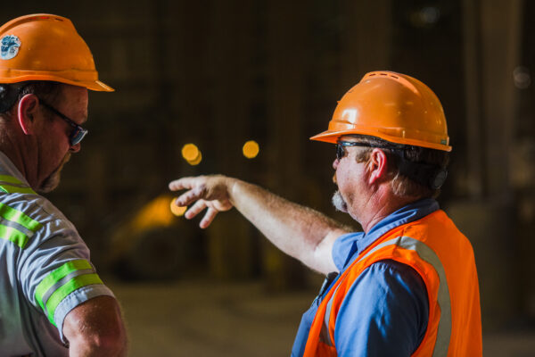 Two men wearing orange hard hats working in a construction setting