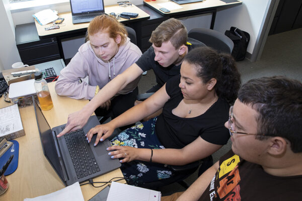 Four students gather around laptop computer