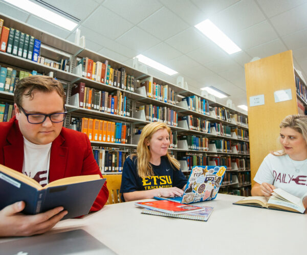 Students studying at university library with books open